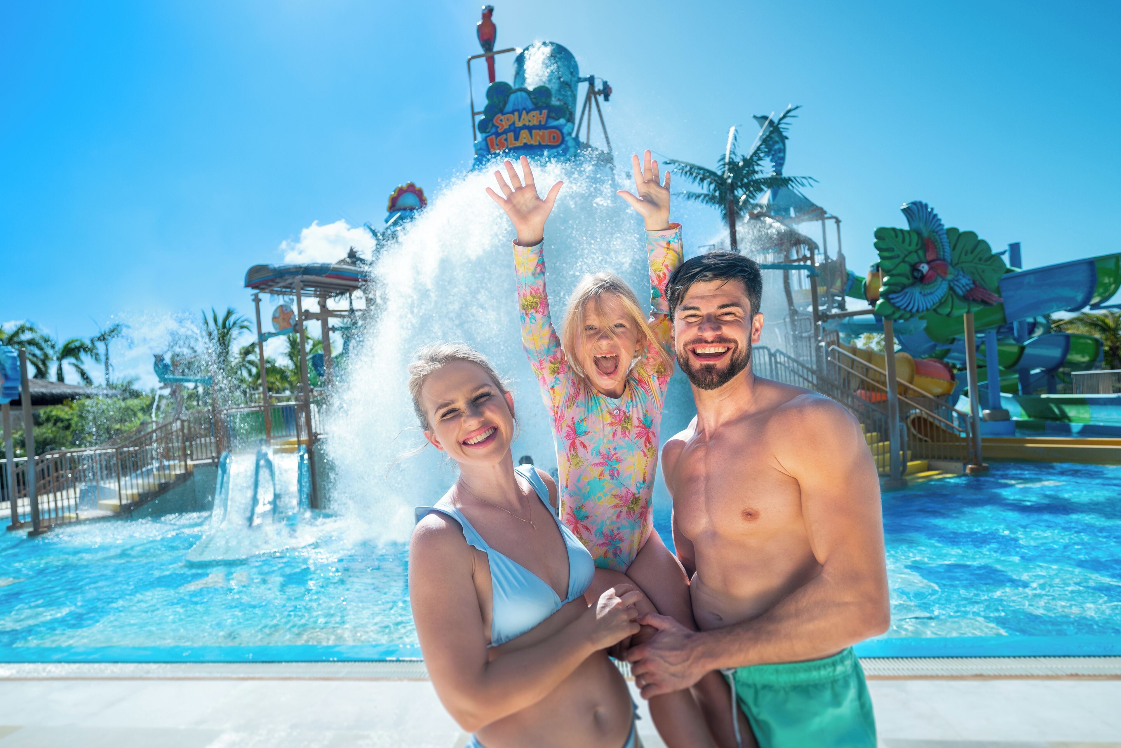 Una familia disfrutando de un parque acuático con una torre de salpicaduras y toboganes al fondo.