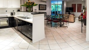 Una cocina moderna con una isla central, comedor con sillas y un televisor en la sala.