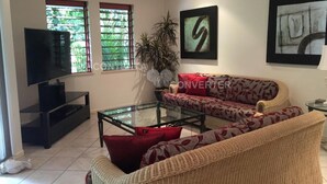 Una sala de estar con un sofá, una mesa de centro, un televisor y dos ventanas con persianas.