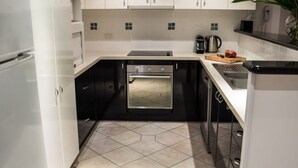Cocina compacta con armarios blancos, horno de acero inoxidable y piso de baldosas.