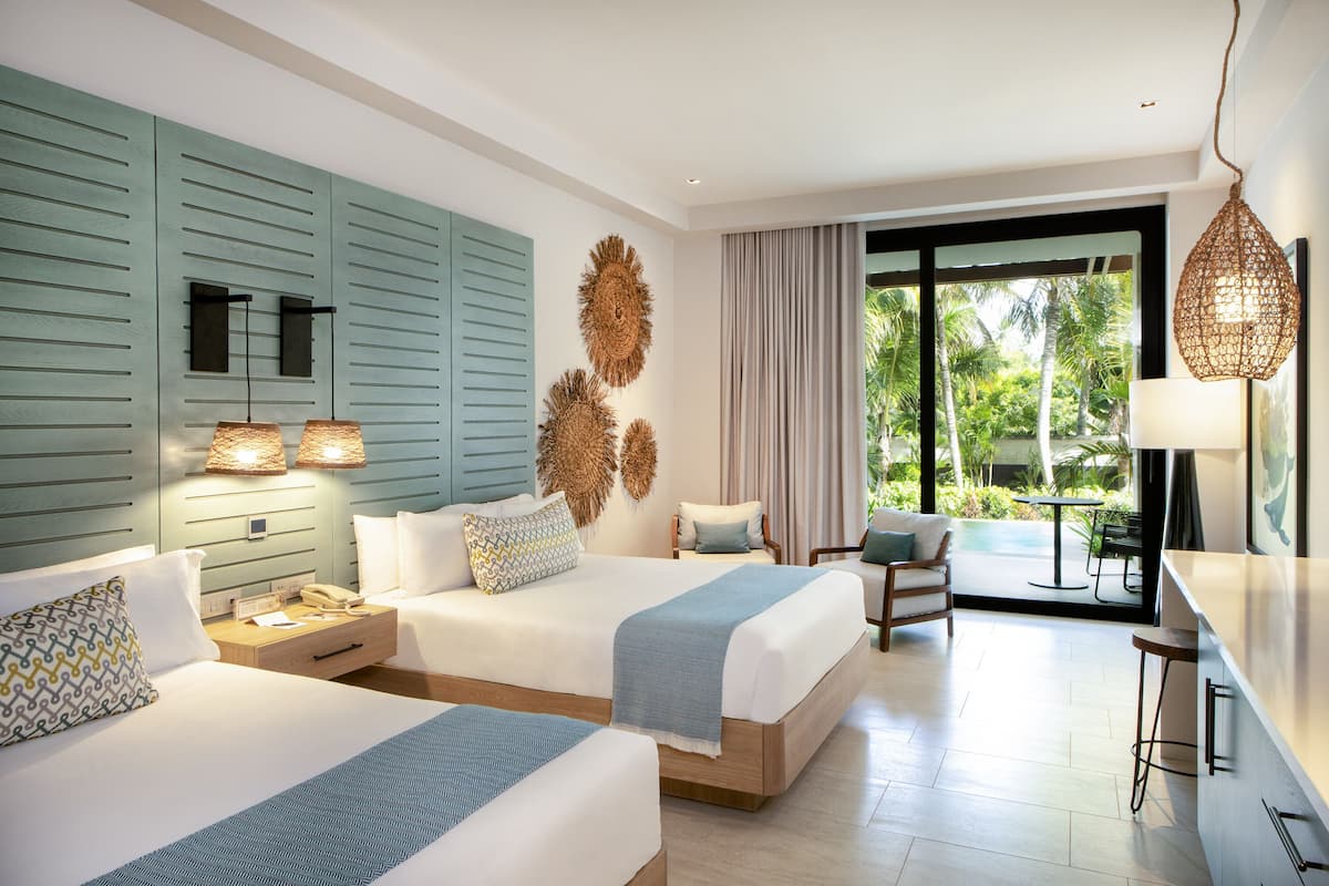 A hotel room with two beds, a desk, and a view of the outdoors.