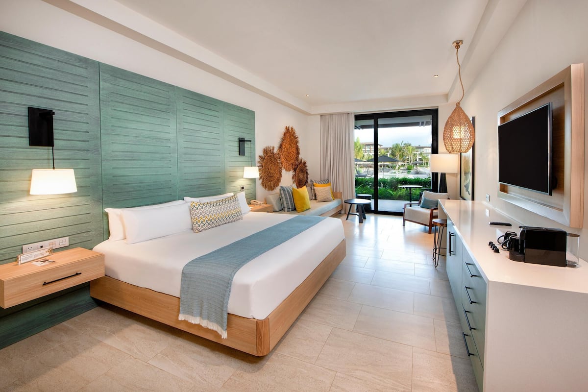A modern hotel room with a large bed, a TV, a desk, and a view of the outdoors.