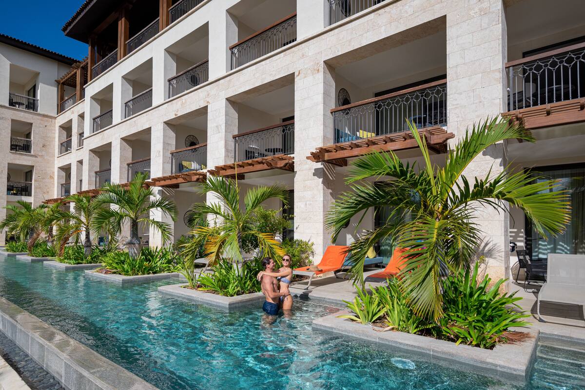 Ein Hotelpoolbereich mit klarem Wasser, Palmen und Liegestühlen.