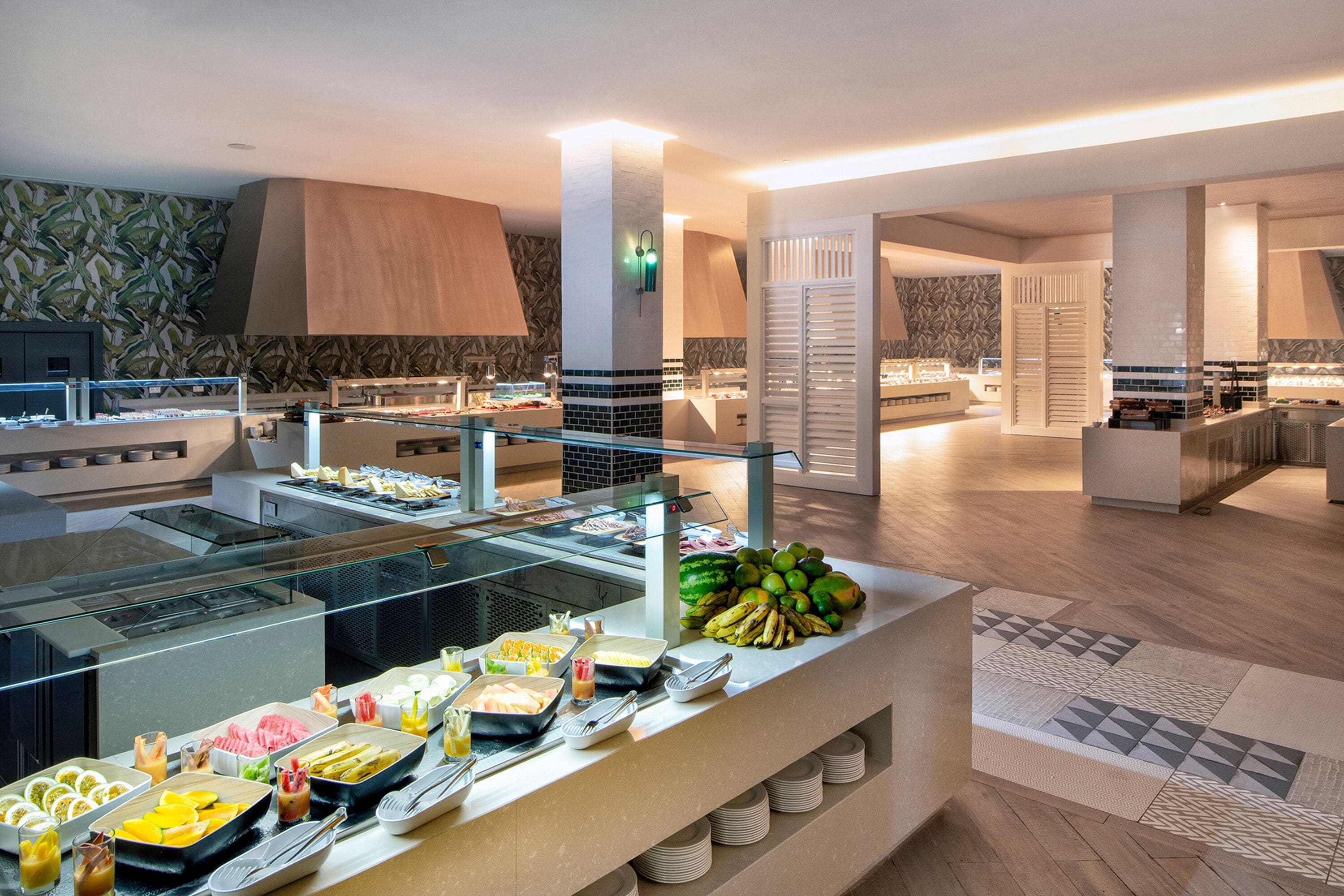 Zona de bufé con diversas opciones de comida y una exhibición de frutas.