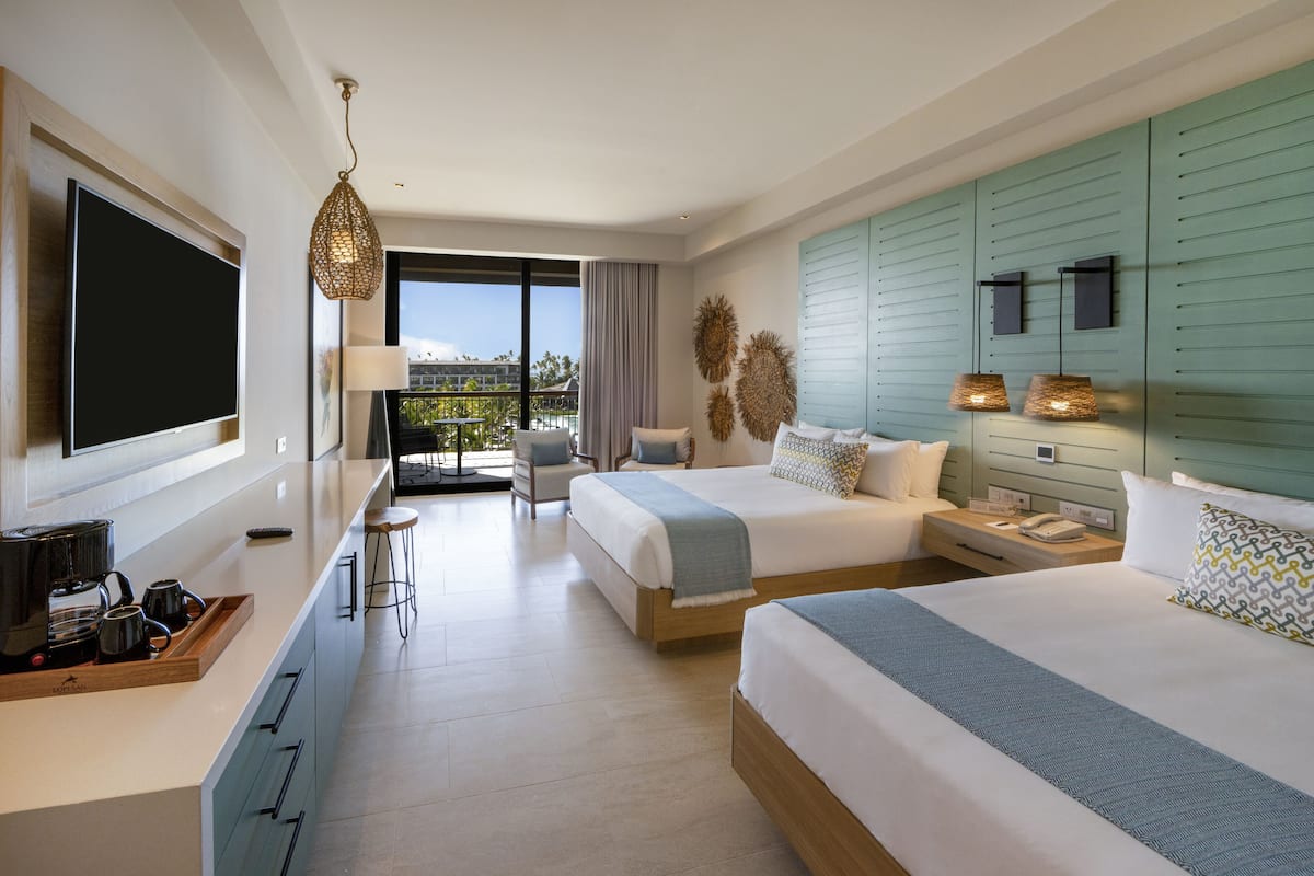 Ein modernes Hotelzimmer mit zwei Betten, einem großen Fernseher, einem Balkon und einer Frühstückstheke.