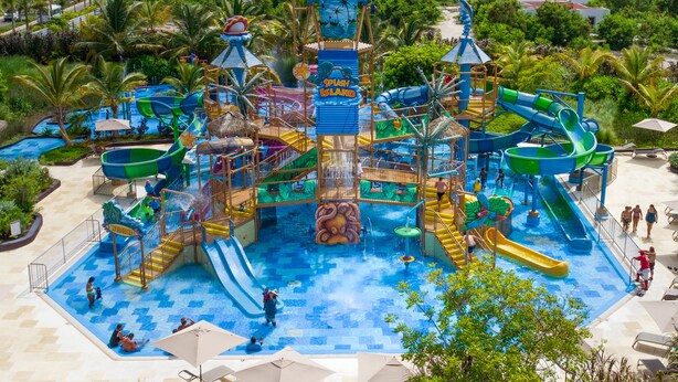 Een waterpark met glijbanen en waterattracties, omringd door palmbomen en een zwembad.