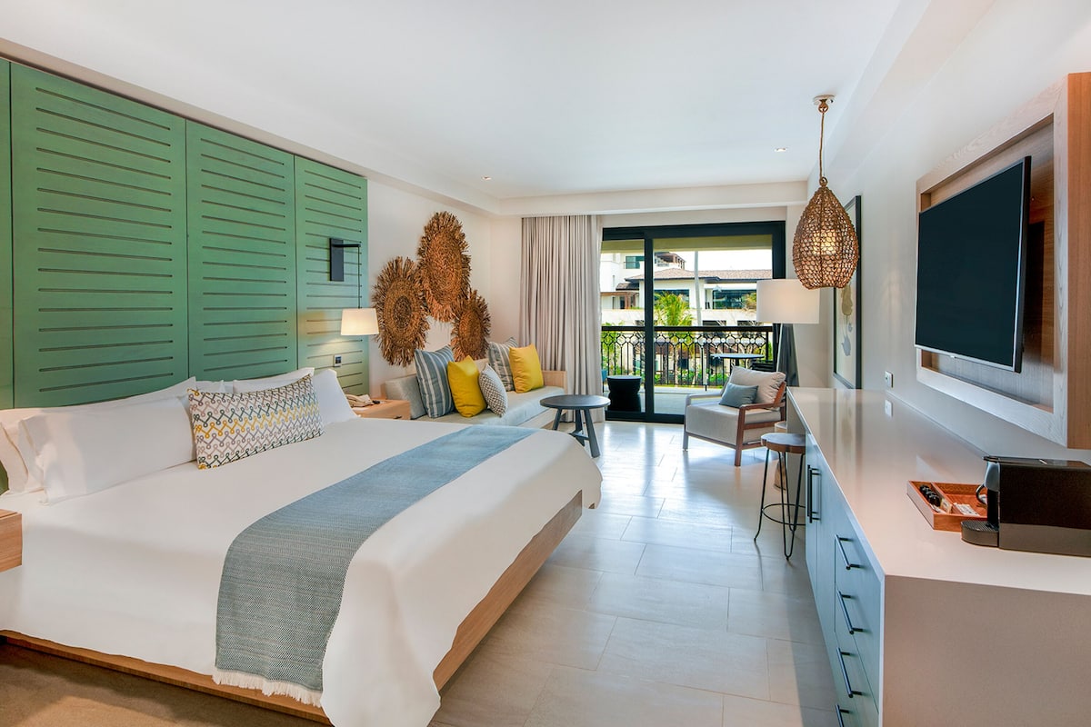 Ein modernes Hotelzimmer mit einem großen Bett, einer kleinen Sitzecke, einem Balkon mit Blick und einem an der Wand befestigten Fernseher.