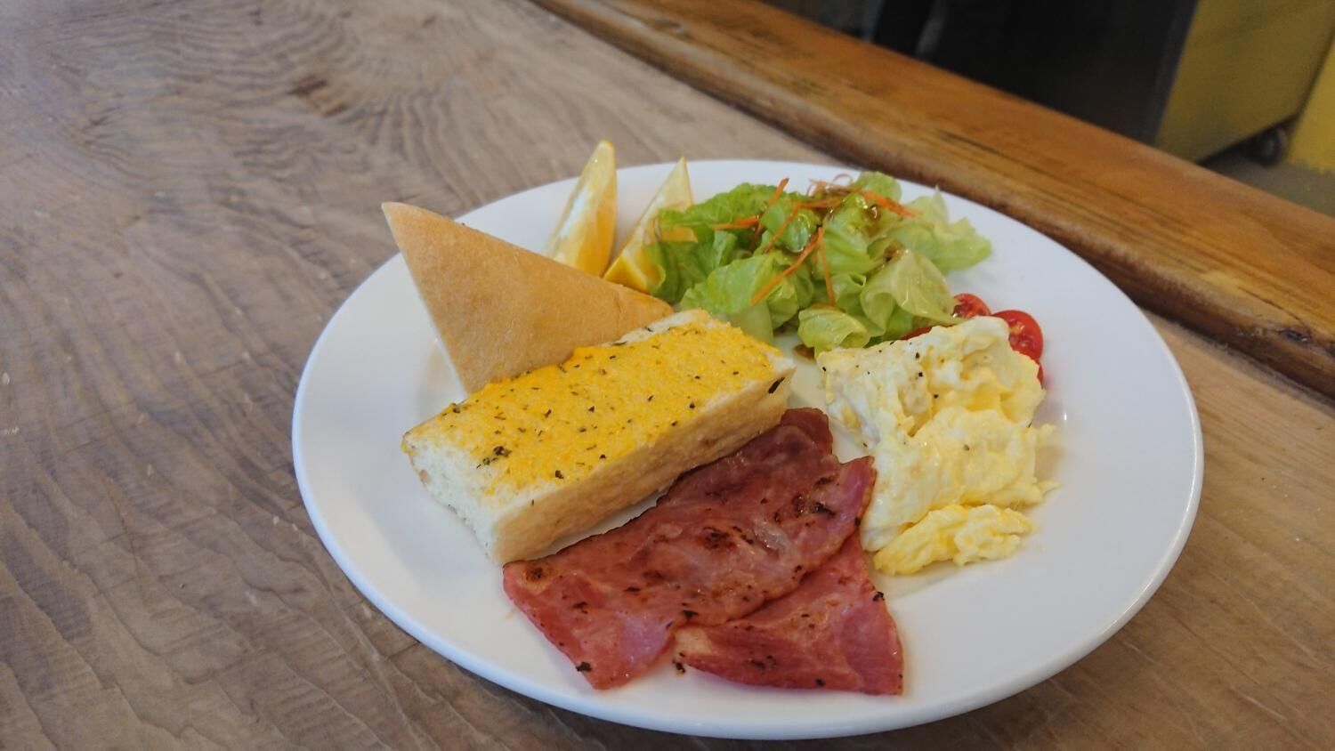 Un plato con tostadas, huevos revueltos, jamón y una ensalada sobre una mesa de madera.
