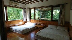 Ein Zimmer mit zwei Betten, Holzwänden, großen Fenstern mit Vorhängen und einem kleinen Tisch mit einer Lampe.