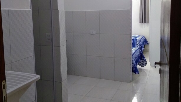 Un baño con paredes de azulejos blancos, una zona de ducha y una pequeña alfombra en el suelo.