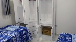 Un dormitorio con un armario blanco, dos camas con ropa de cama de estampado azul y una cortina gris.