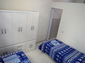 Quarto com duas camas de solteiro, um guarda-roupa e um espelho.