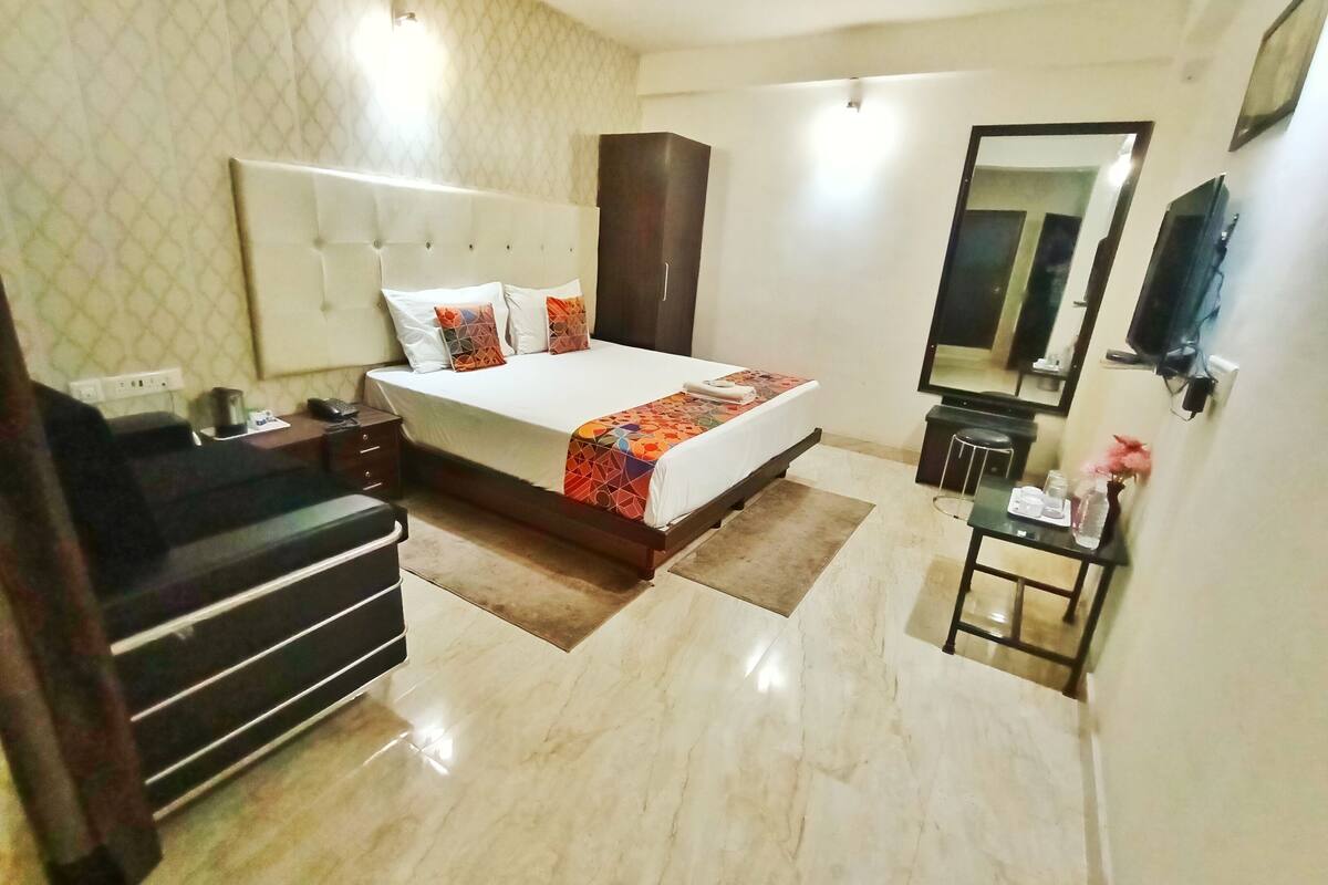 A hotel room with a large bed, a nightstand, a dresser, a mirror, and a small table with a vase and a tray.