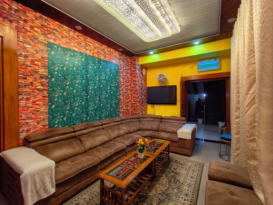 Un salón con un sofá de cuero marrón, una mesa de centro de madera con un centro de mesa floral, un tapiz estampado, una pared de ladrillo con un tapiz floral y una pared amarilla con un reloj y una televisión.