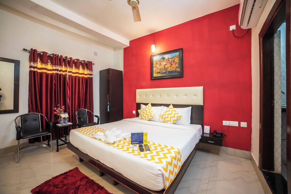 A hotel room with a large bed, red walls, a ceiling fan, and a painting on the wall.