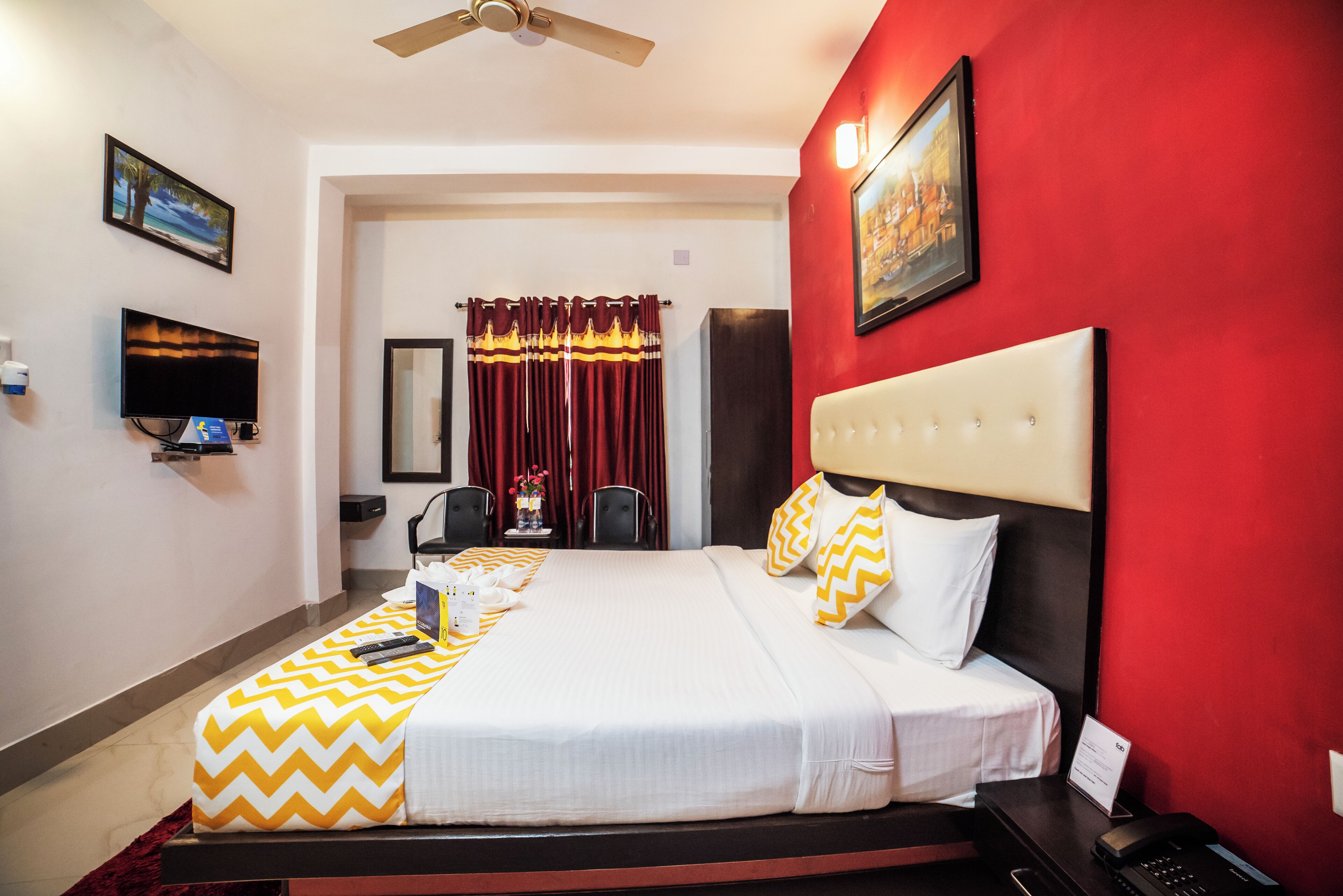 A hotel room with a large bed, a television, a desk with a phone, and a red accent wall.