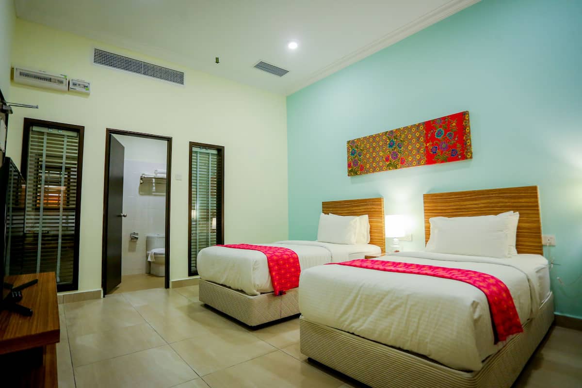A hotel room with two beds, a wooden headboard, a red and blue artwork on the wall, and a bathroom with a toilet and sink.