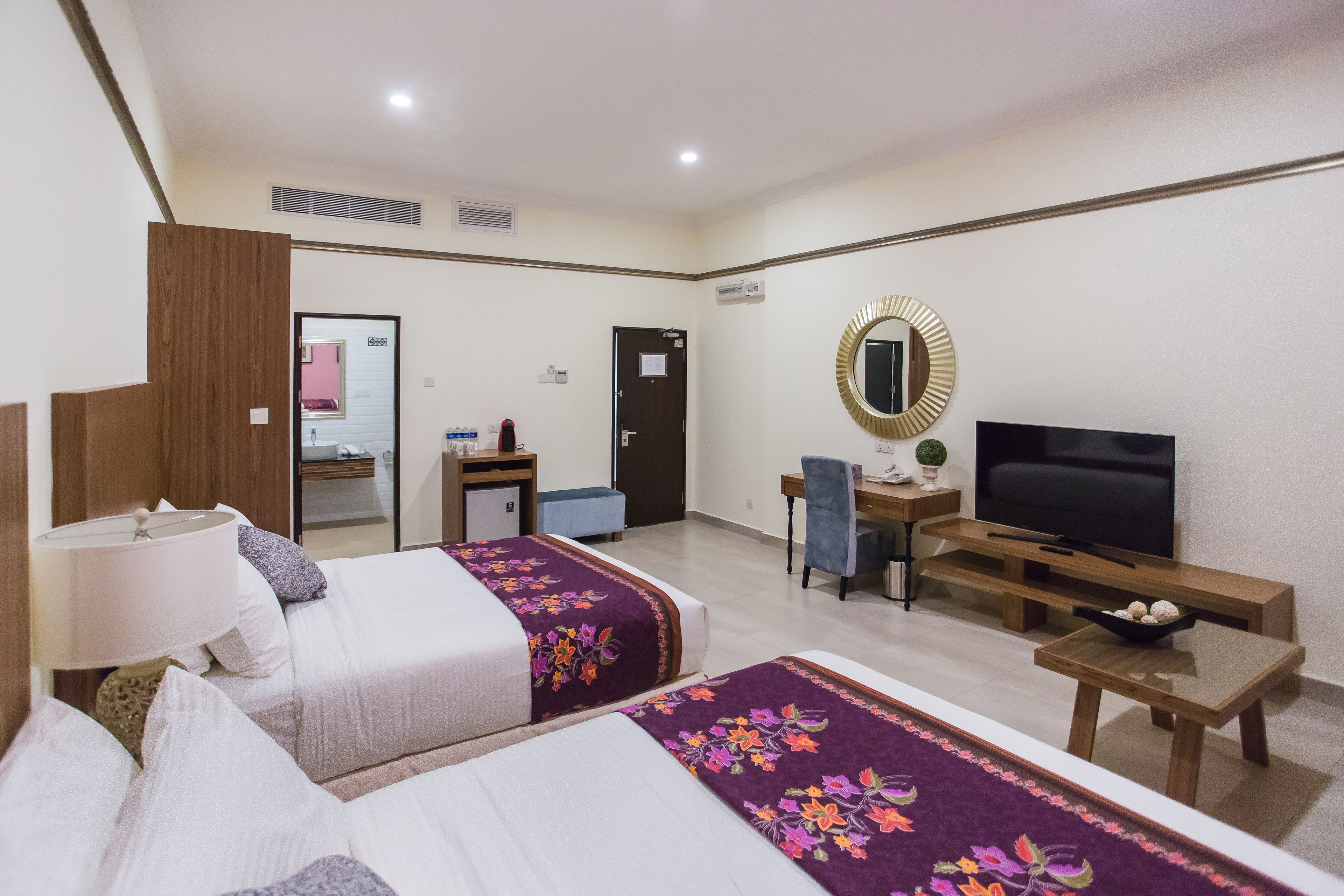 A hotel room with two beds, a desk, a television, and a mirror.