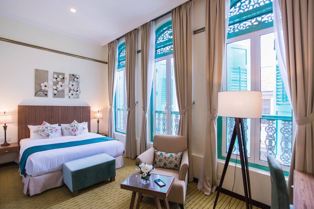 A hotel room with a bed, a chair, a table, and a window with curtains.