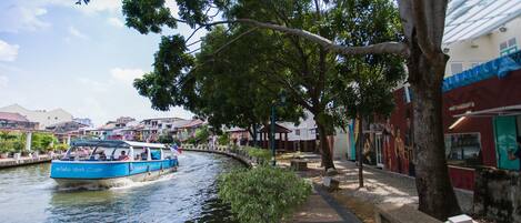 A boat on a river, a tree-lined pathway, and buildings in the background.