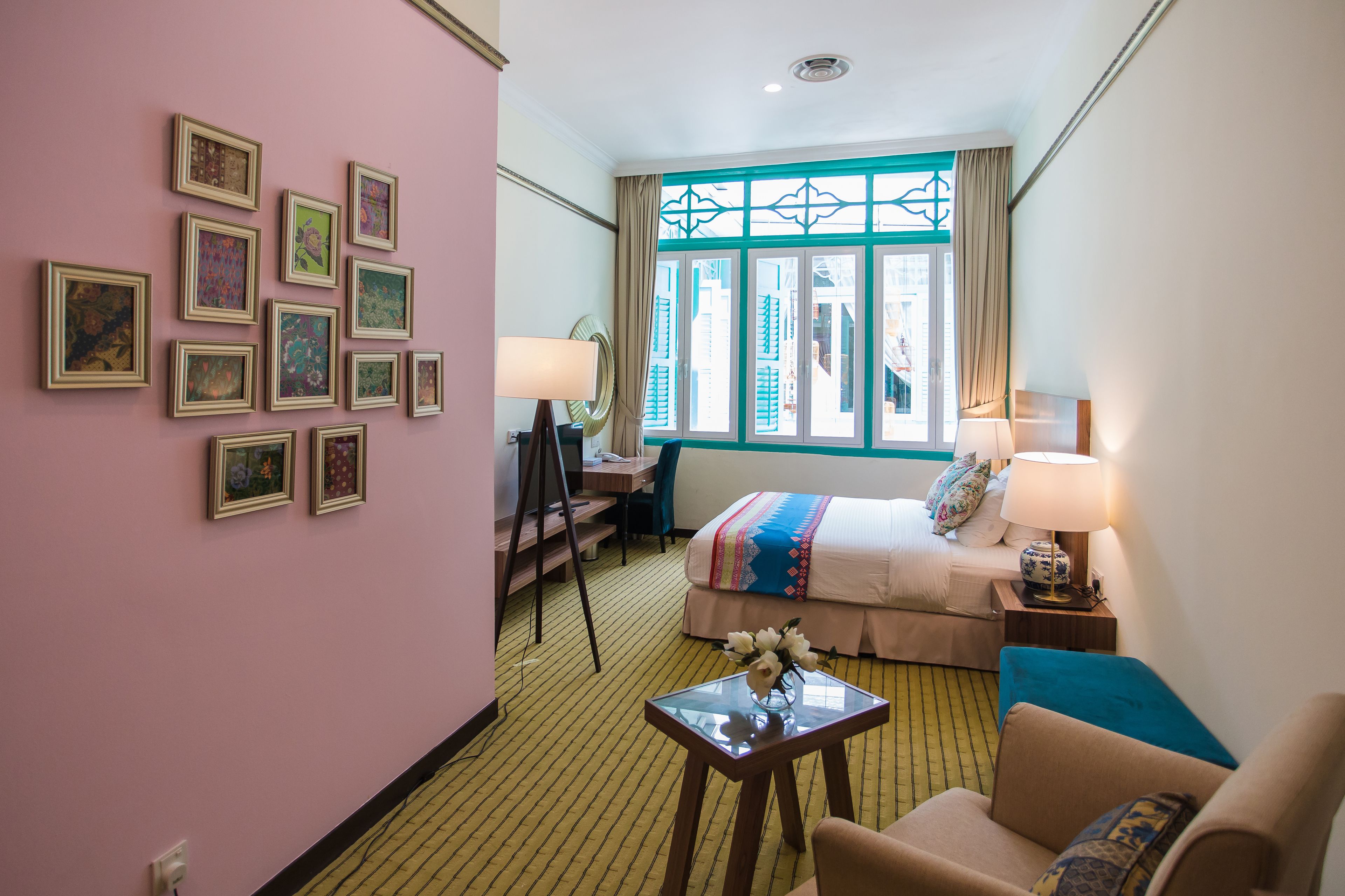 A hotel room with a bed, two bedside tables, a desk, a chair, a small table with a vase, and a wall with framed pictures.