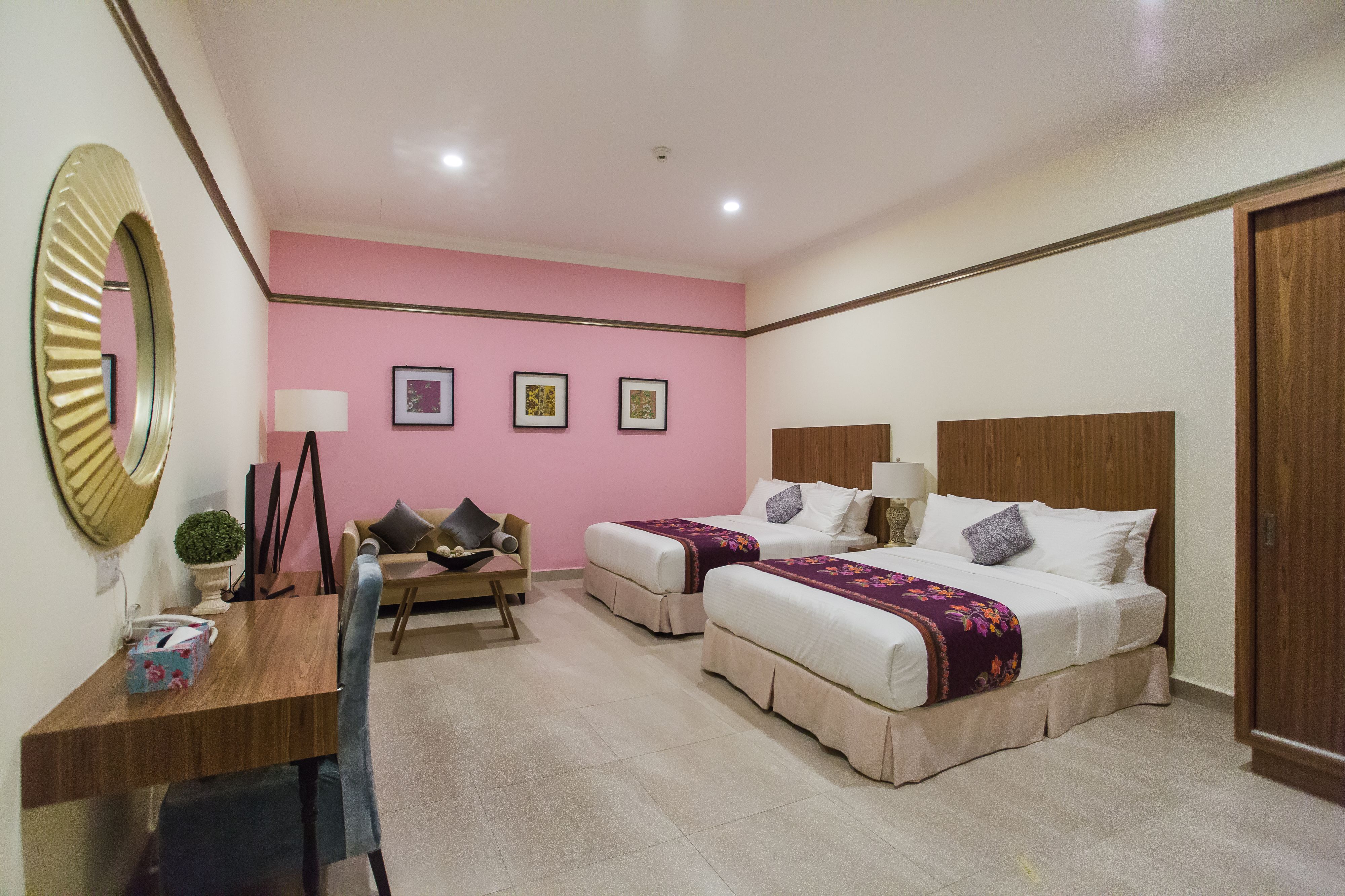 Habitación de hotel con dos camas, un escritorio, una silla, un espejo y una pared con tres cuadros enmarcados.