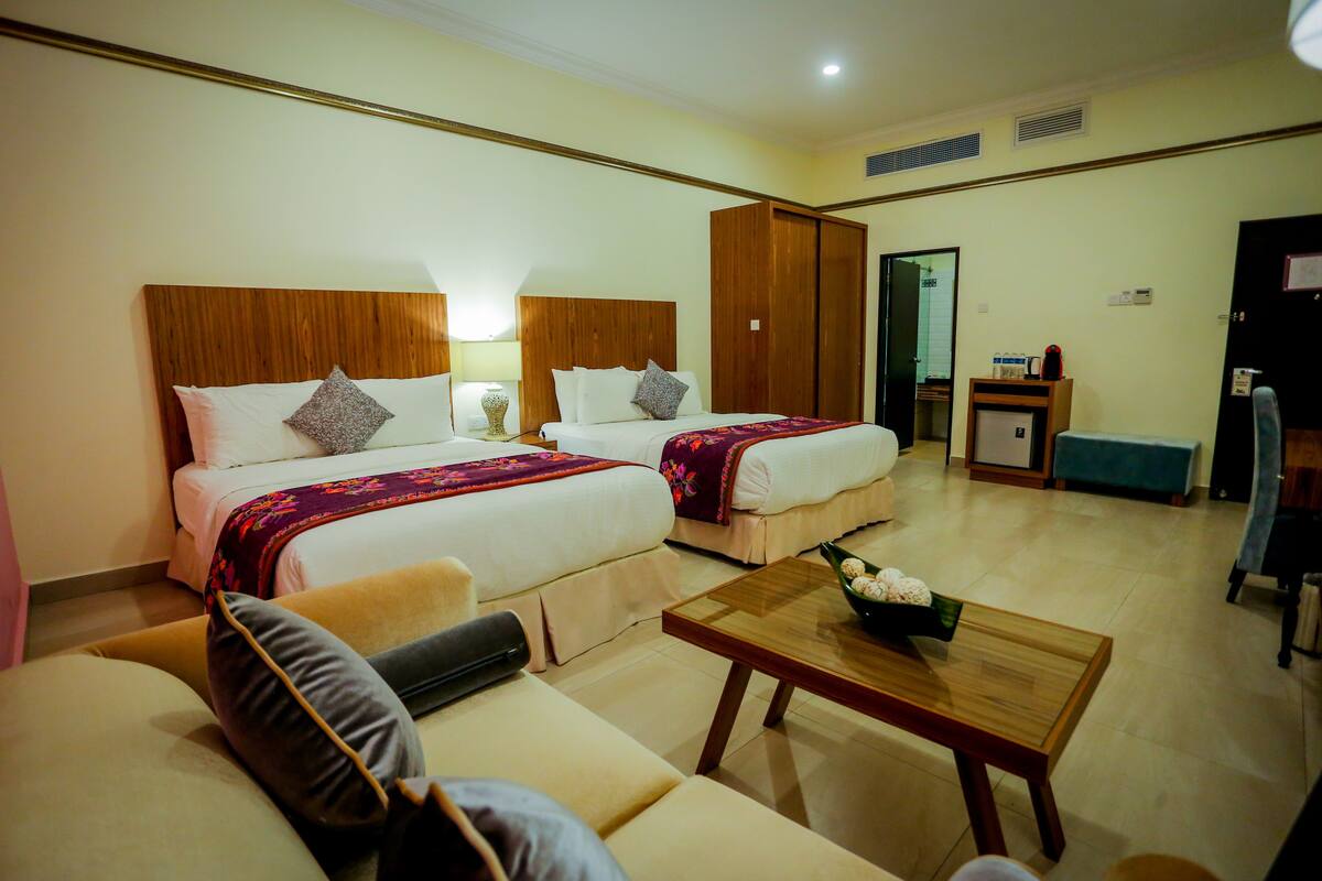 A hotel room with two beds, a sofa, a wooden coffee table, and a small desk with a chair.