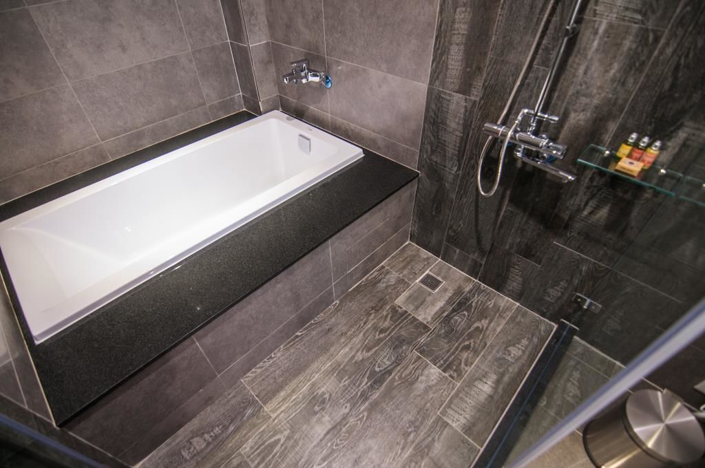 Un baño moderno con una bañera independiente, cabina de ducha con mampara de vidrio y suelo de baldosas oscuras.
