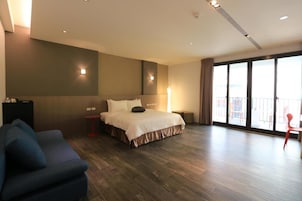 Habitación de hotel moderna con una cama grande, un sofá, un televisor y un balcón con vistas.