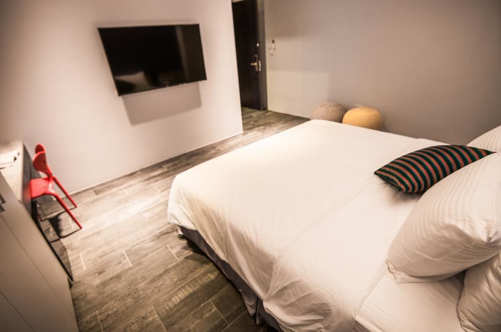 Un dormitorio con una cama, un televisor montado en la pared y una silla roja.