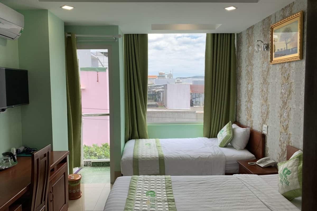 Ein Hotelzimmer mit zwei Betten, einem Schreibtisch, einem Fernseher und Blick auf Gebäude durch das Fenster.