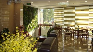 Un hall d’hôtel doté d’un ventilateur de plafond, d’un lustre, d’un espace salon avec un canapé et des fauteuils, d’un escalier et offrant une vue sur l’extérieur grâce à de grandes fenêtres.