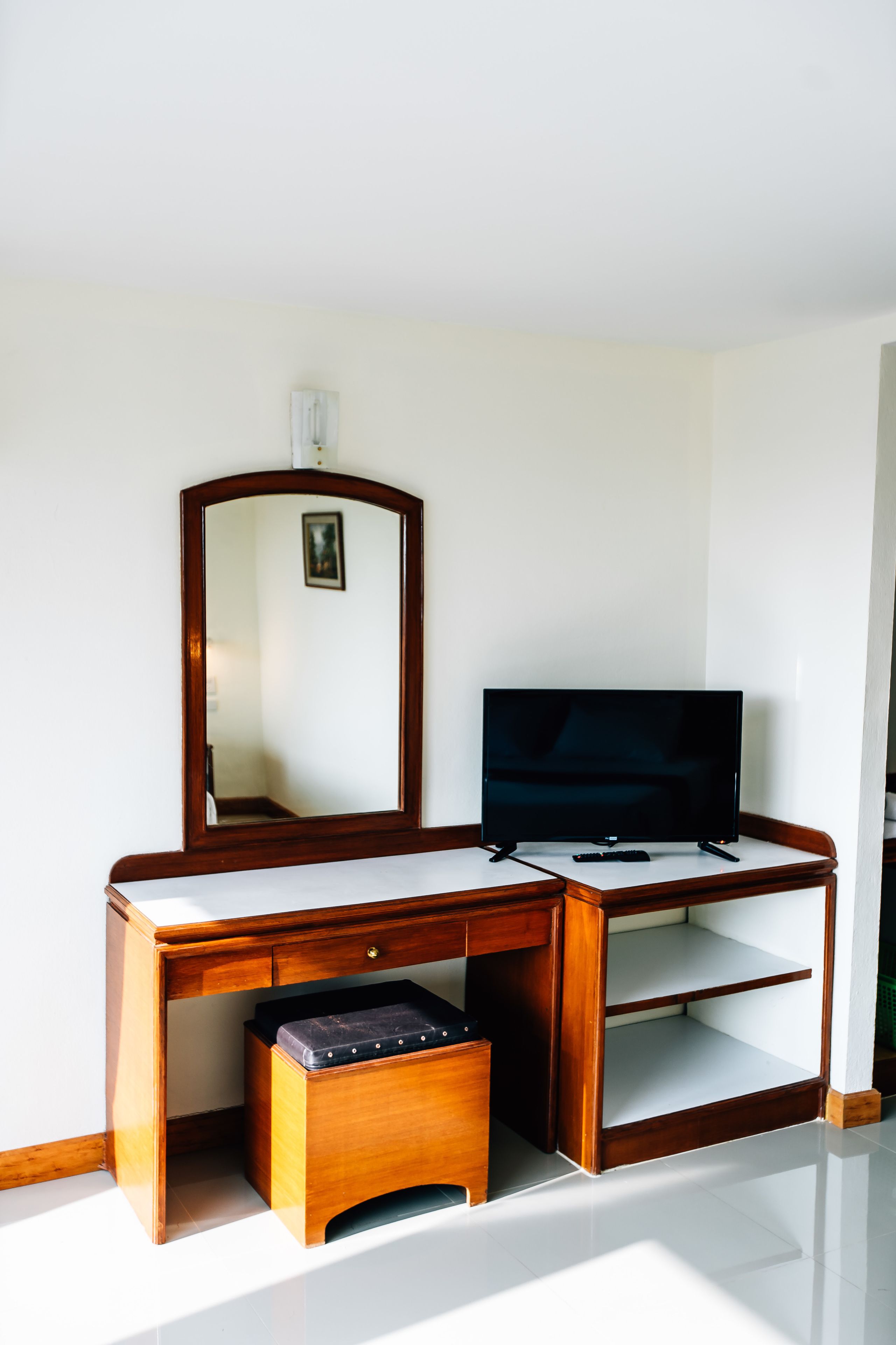 Un bureau en bois, avec une télévision, un miroir et un petit tabouret.