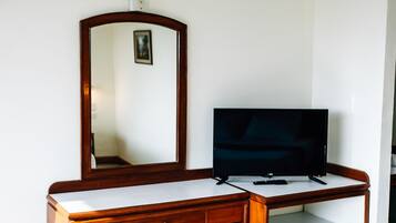 Un bureau en bois, avec une télévision, un miroir et un petit tabouret.