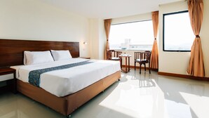 Una habitación de hotel con una cama grande, una mesita con sillas y un ventanal con cortinas.