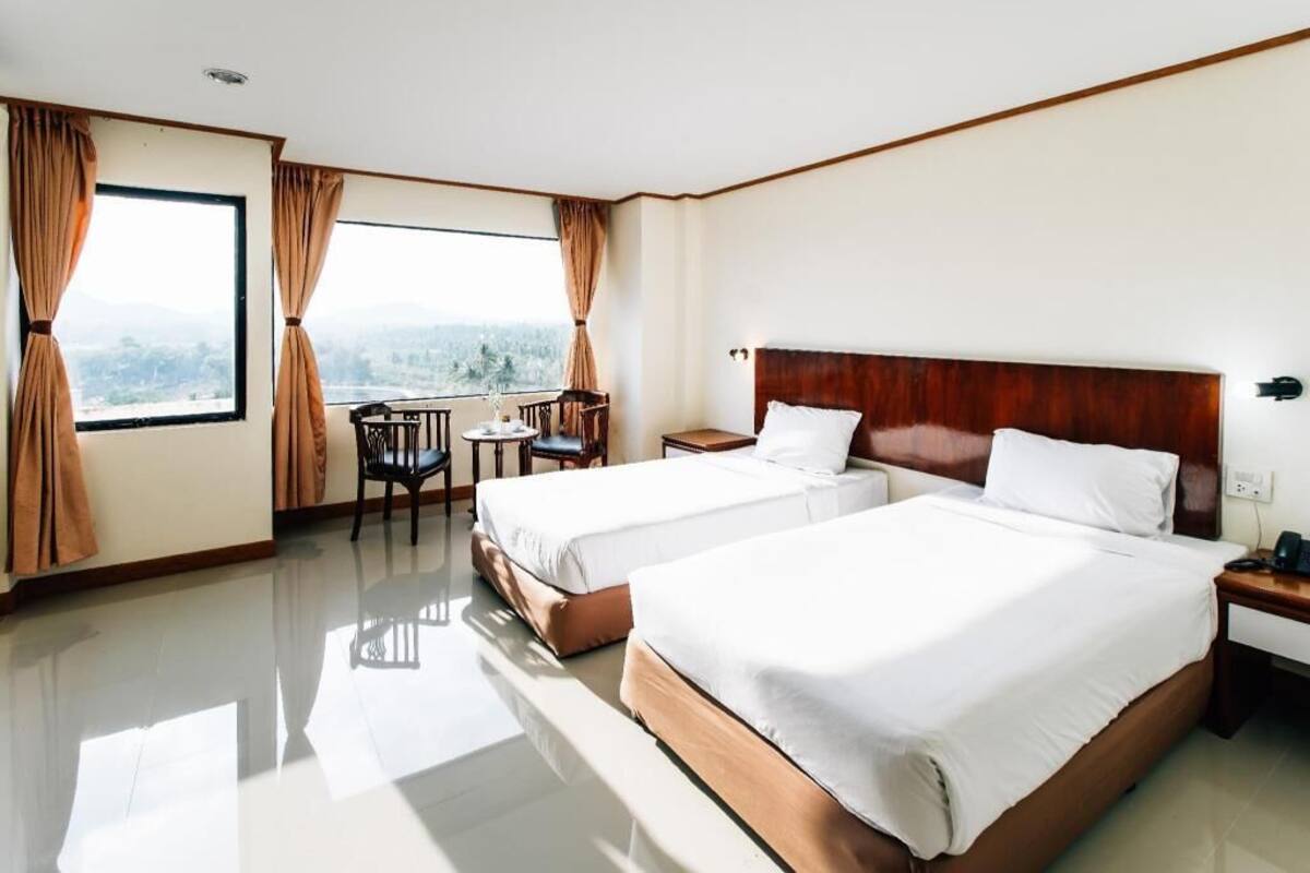 A hotel room with two beds, a small table, a chair, and a window with curtains.