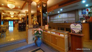 Un vestíbulo de hotel con mostrador de recepción, área de recepción para cajeros y un jarrón grande con flores.
