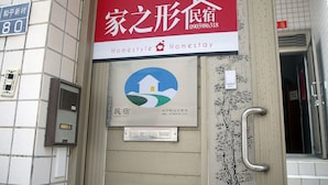 A hotel entrance with a red and white sign indicating 'Homestyle Homestay' and a blue logo with a house on a hill. - HomestyleHomestay (Jincheng)