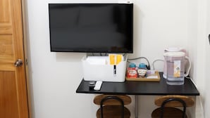 A small workspace with a flat-screen TV, a white organizer with stationery, a water pitcher, and a remote control. - HomestyleHomestay (Jincheng)