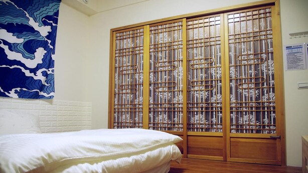 A bedroom with a bed, a wooden sliding door with bamboo patterns, and a blue abstract wall hanging. - HomestyleHomestay (Jincheng)