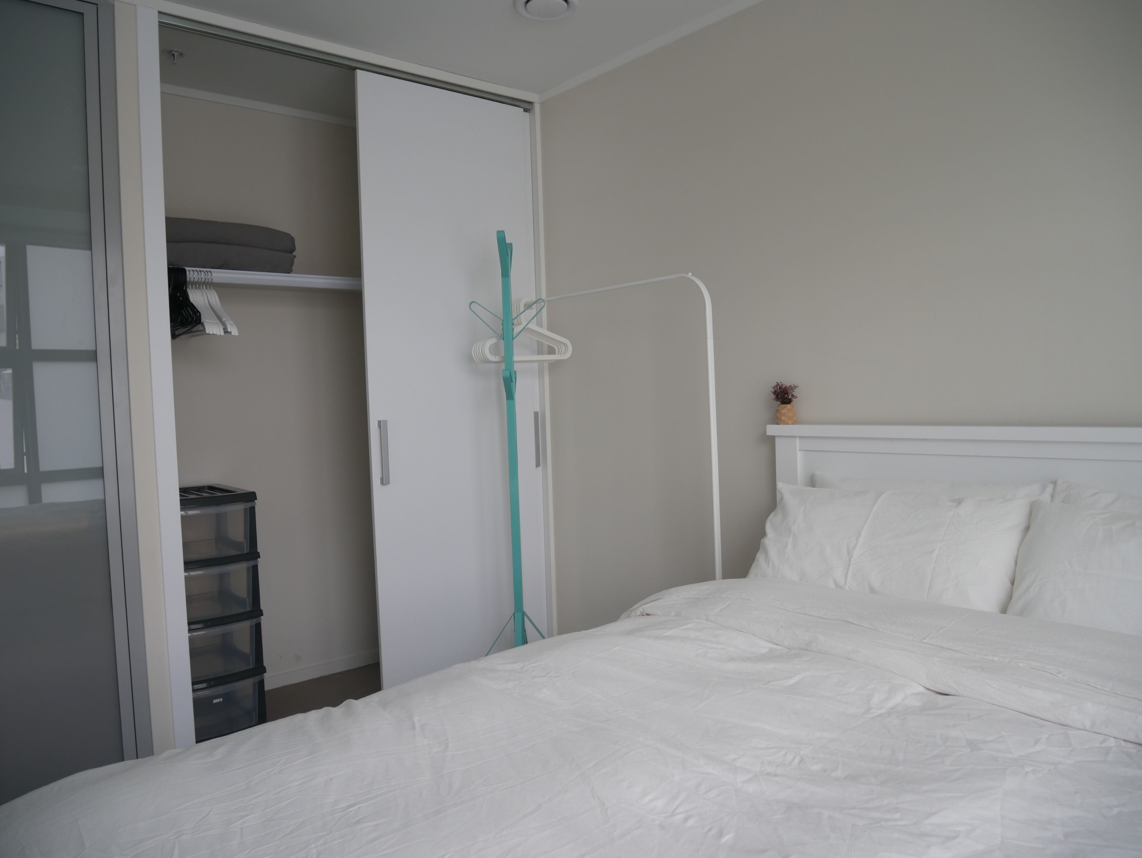 Un dormitorio con una cama, un armario blanco y una estantería con una planta pequeña.