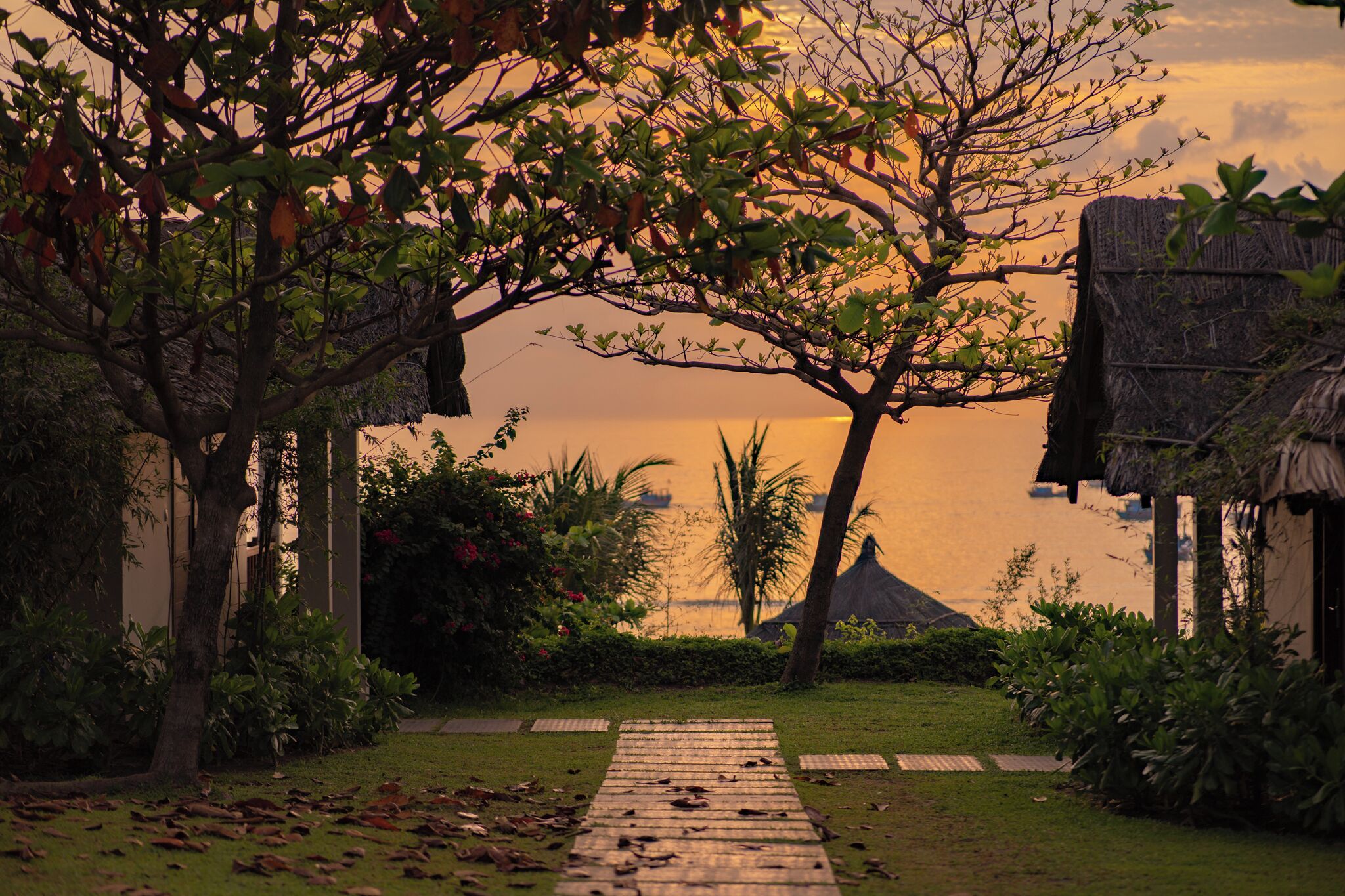 A pathway leading to a thatched-roof structure with a view of the water.