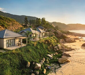 A coastal property with multiple houses, a sandy beach, and a rocky hillside. - Crown Retreat Quy Nhon (Cat Tien)