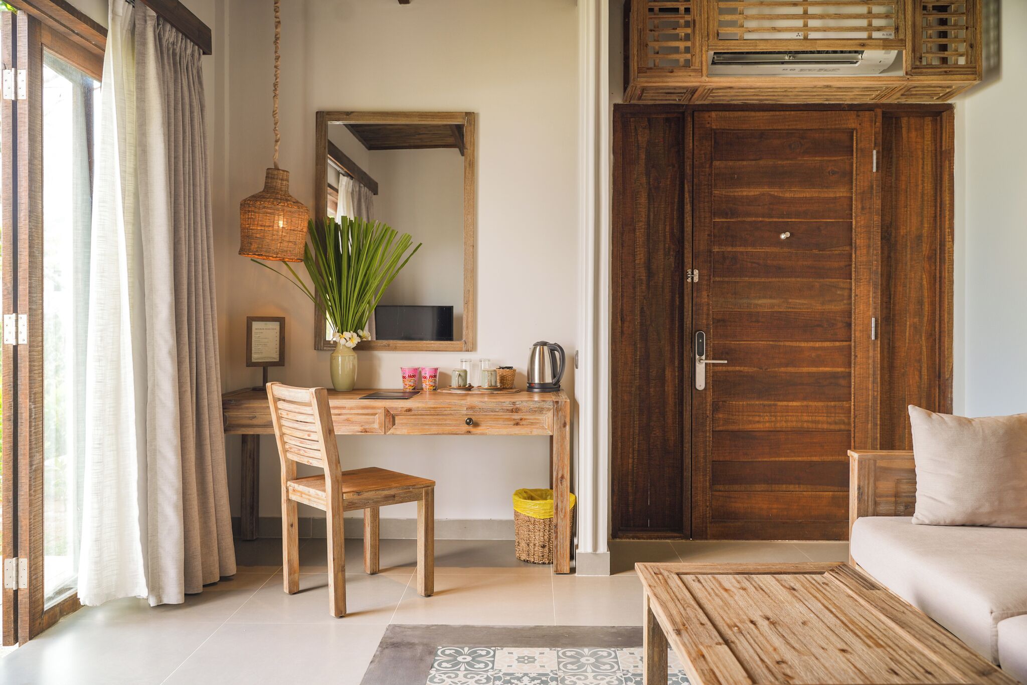 A room with a wooden desk, chair, and sofa, a large wooden door, and a hanging light fixture.