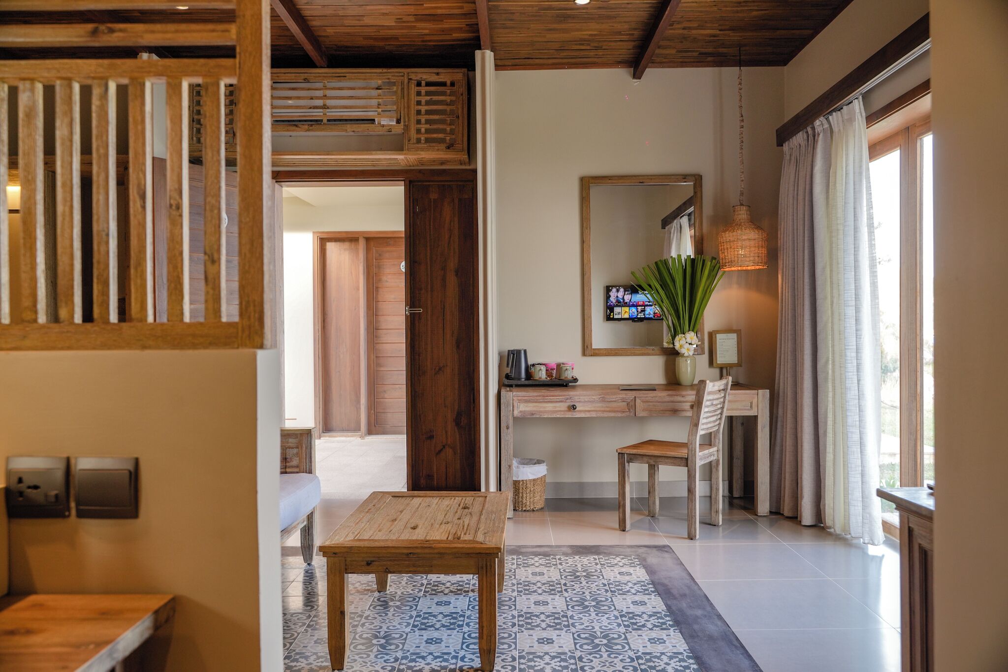 Una habitación con un escritorio de madera, una silla, una mesita, un espejo y un televisor.