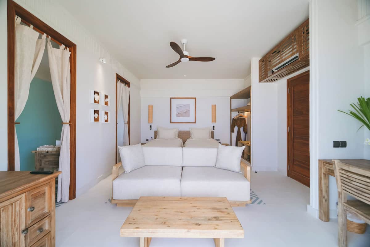Une chambre à coucher avec un grand lit, un ventilateur de plafond, une commode en bois et une petite table.