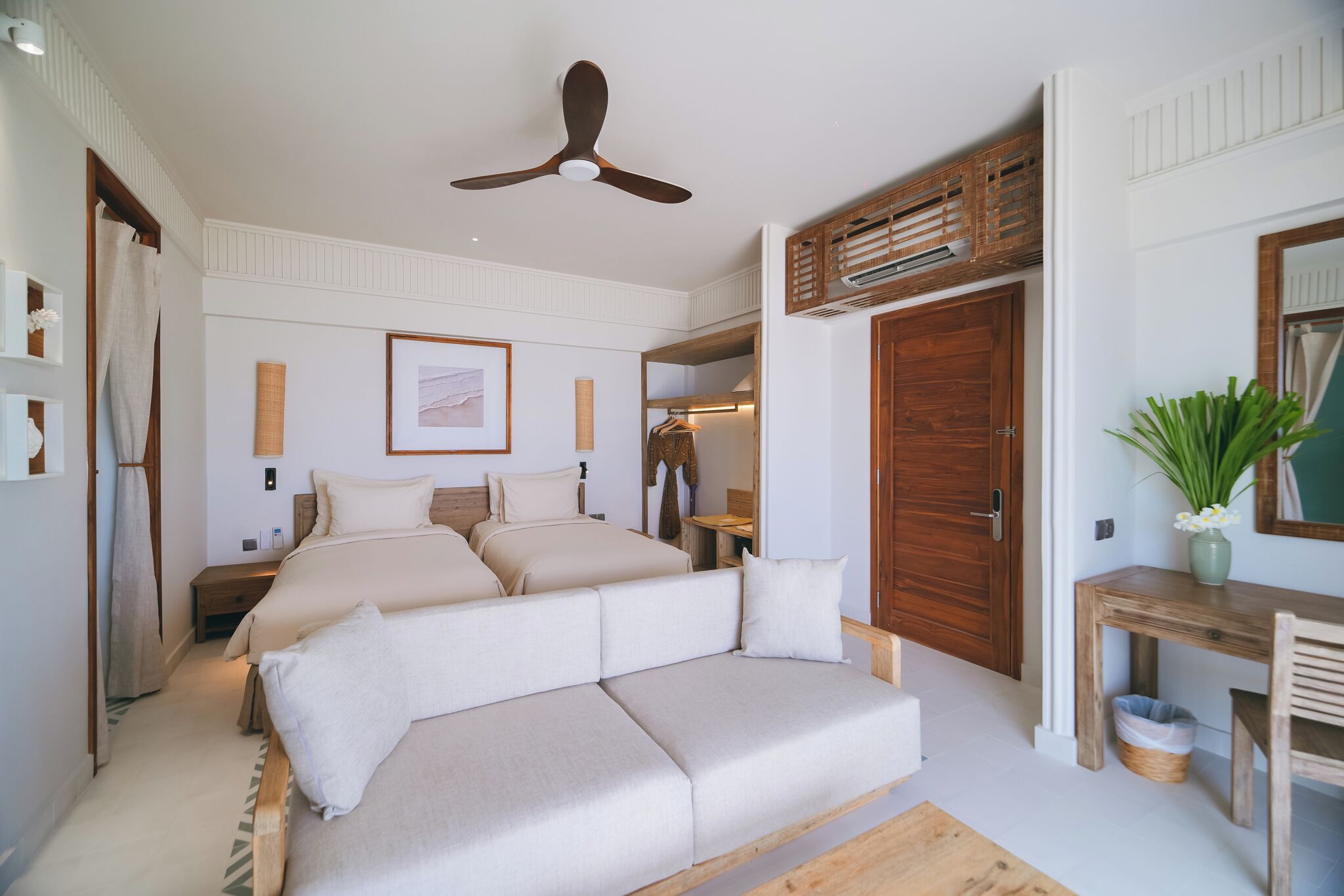 Ein Schlafzimmer mit einem großen Bett, einem Deckenventilator, einem Holzschrank und einem kleinen Tisch mit einer Pflanze.