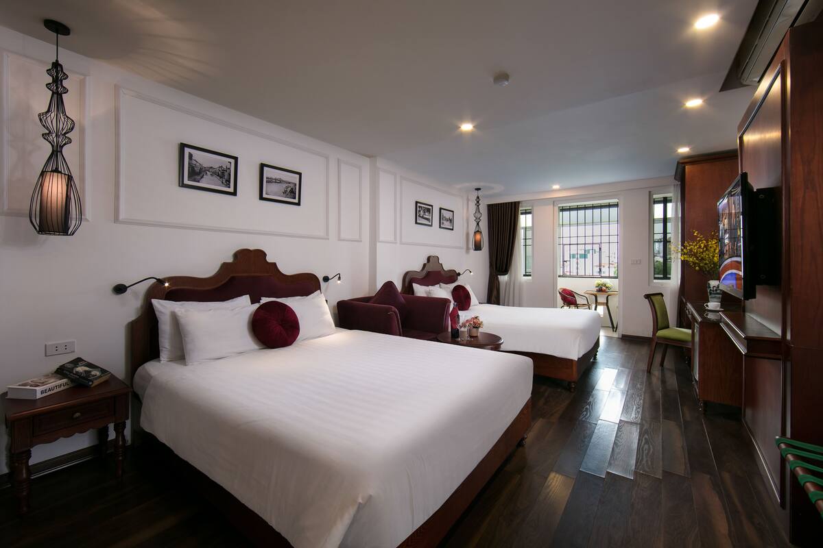 A hotel room with two beds, a wooden headboard, a nightstand, a desk, a chair, and a television.