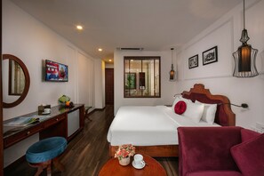 Une chambre d’hôtel avec un lit, un bureau et une chaise, une petite table avec une tasse et des fleurs, et un fauteuil rouge.