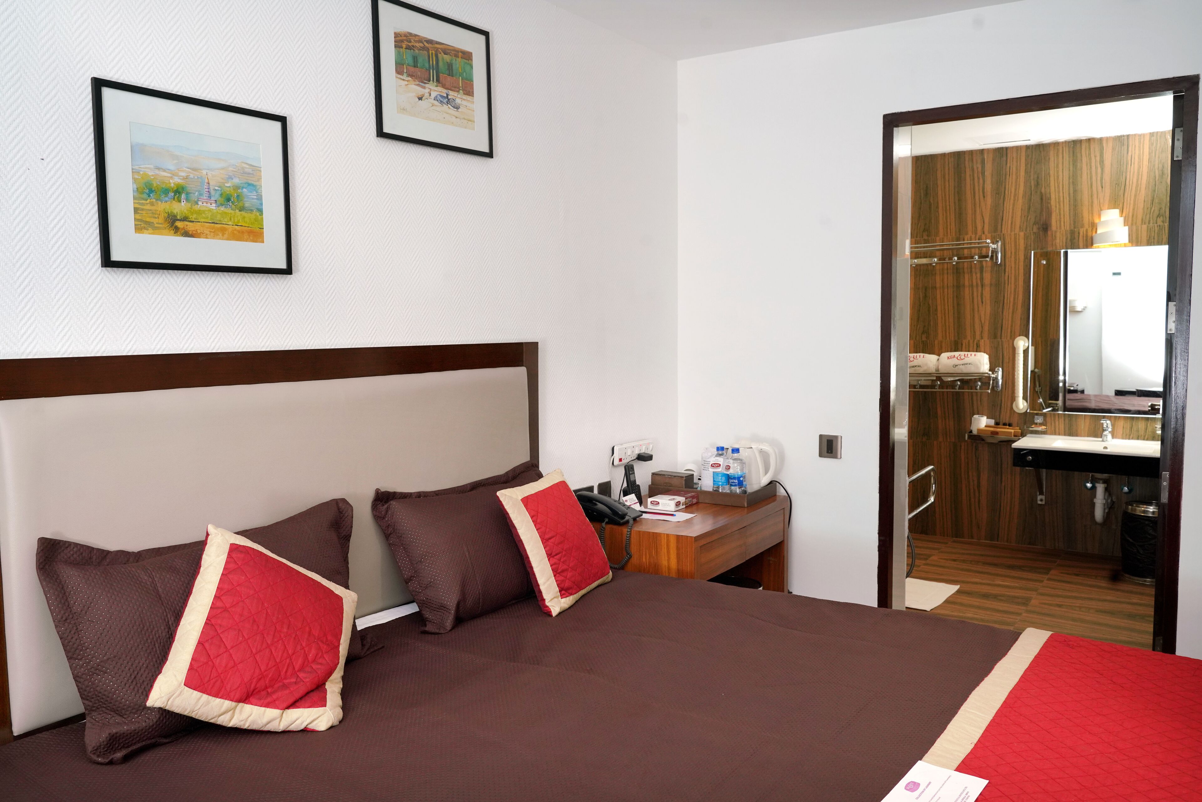 A hotel room with a large bed, two pillows, a bedside table with a phone and a lamp, and a door leading to a bathroom.